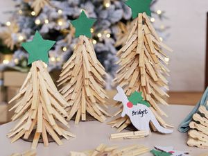 A cardboard kangaroo Christmas table place card with the name ‘Bridget’ written on it, resting in front of miniature wooden peg Christmas trees.