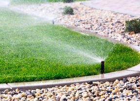 Image of sprinkler system watering grass that meets a stone garden bed