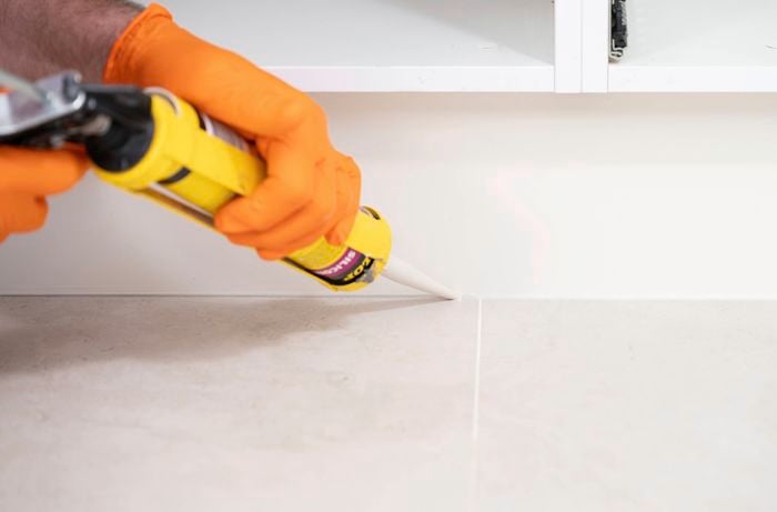 A person wearing orange gloves is sealing the bottom edge of the kickboard with a caulking gun.  