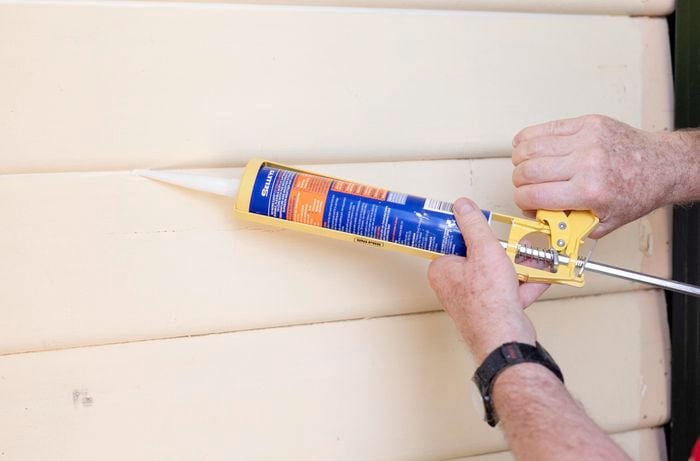 A person filling gaps in weatherboards using gap filler