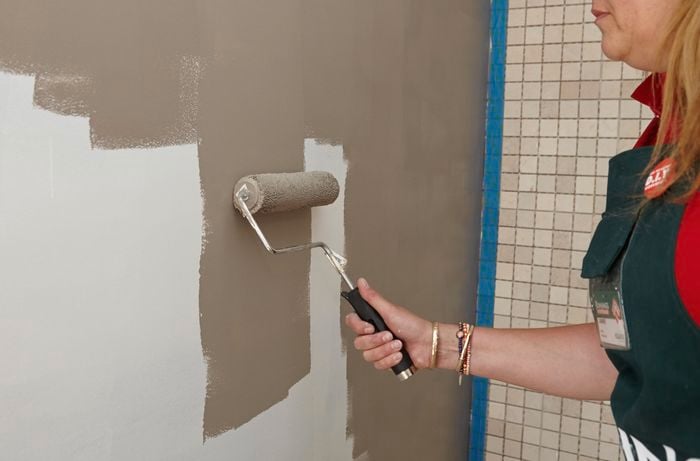 A person painting a plasterboard wall a stone colour using a roller
