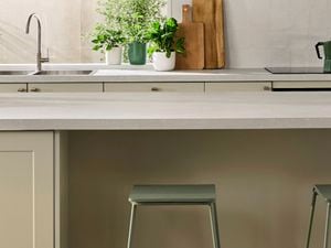 Light green modern kitchen with a white benchtop, green bar stools at the benchtop and white drop down lights.