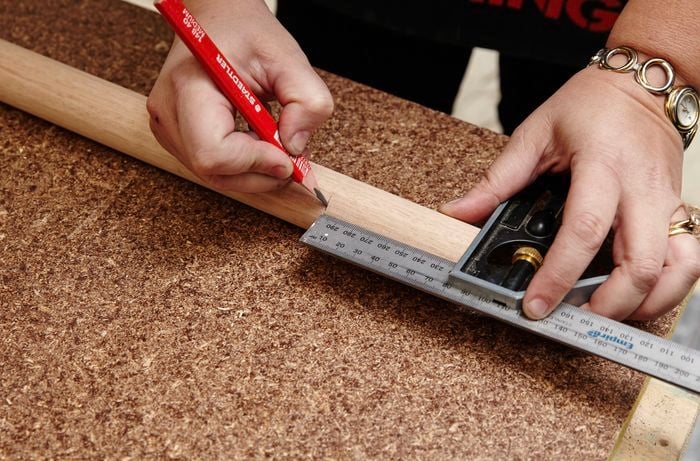 A square rule and pencil being used to mark a piece of timber for cutting