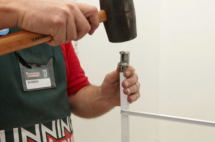 A Bunnings team member using a rubber mallet to tap the wheel bracket into each leg