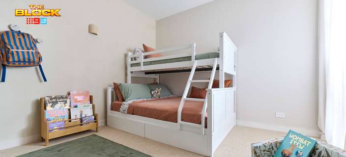 Children’s bedroom featuring a white bunk bed, rust-coloured bedding, book display and soft green rug.