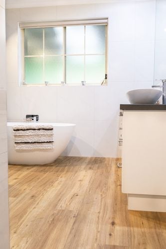 White bathroom with freestanding bath and vinyl plank timber-look floor