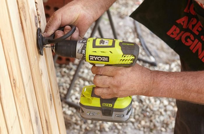 Person drilling hole to fit a ring latch on a gate