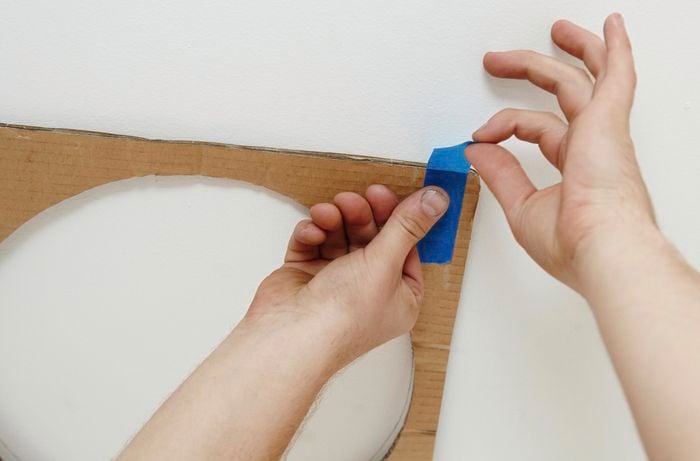 A person taping a cardboard template to a ceiling