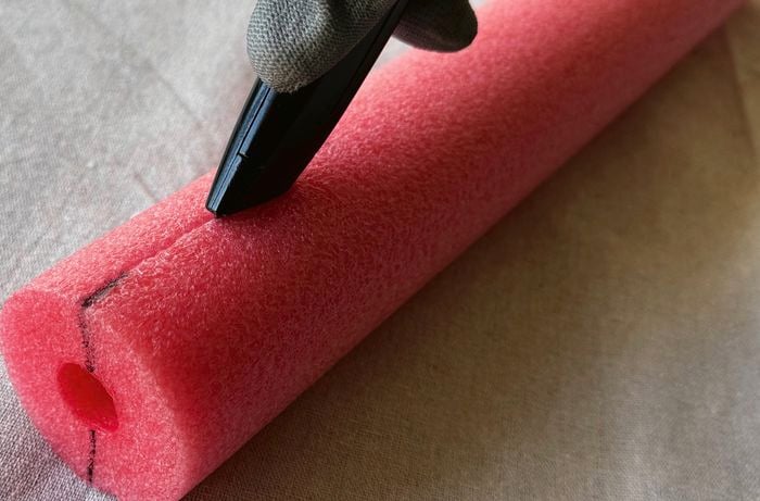 A close up of a red pool noodle marked with a black marker at one end and being cut