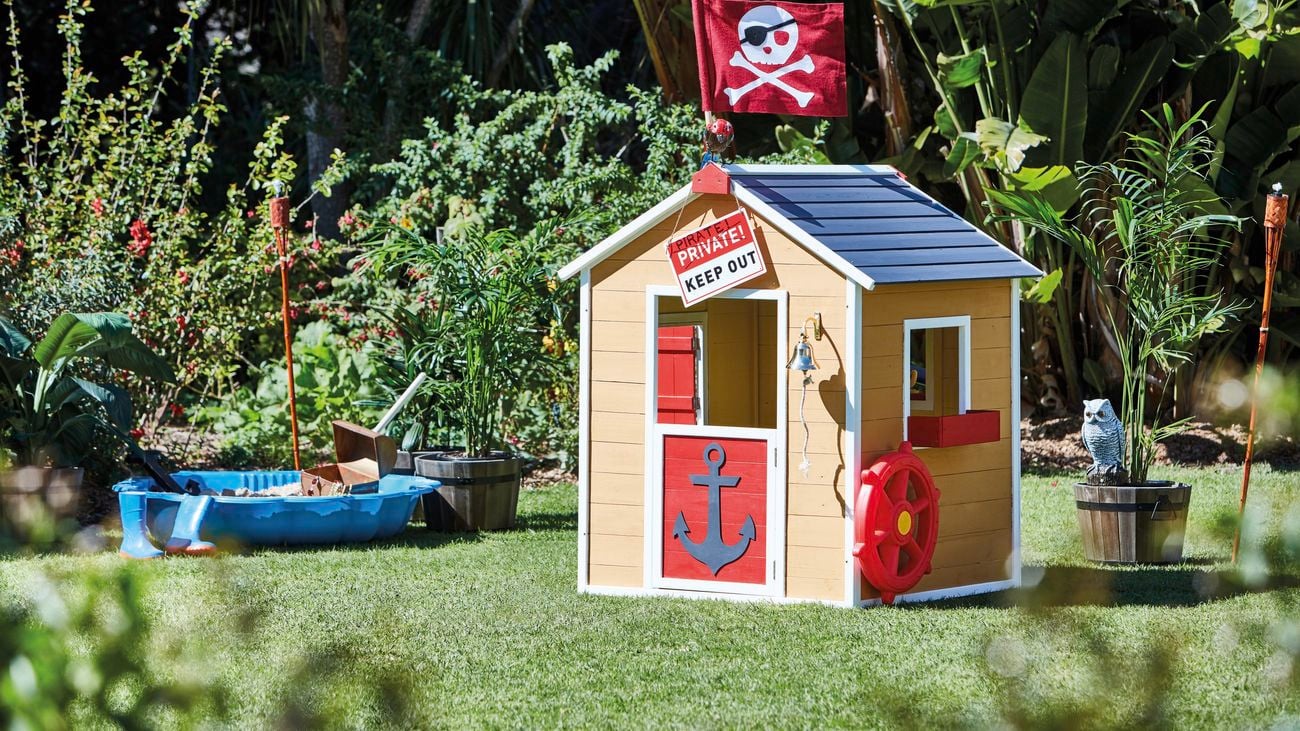 A small brown cubby house in a backyard.