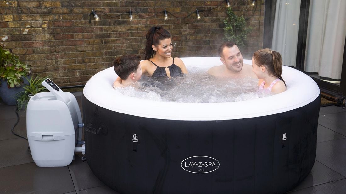Family sit in a spa bath with in their yard with daughter and son and the front and mother and father at the back