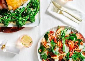Image of a main dish of Turkey Roulade with broccolini and beans with a zesty dressing, a side dish of fresh salad on a white linen table setting with cutlery and drinks.
