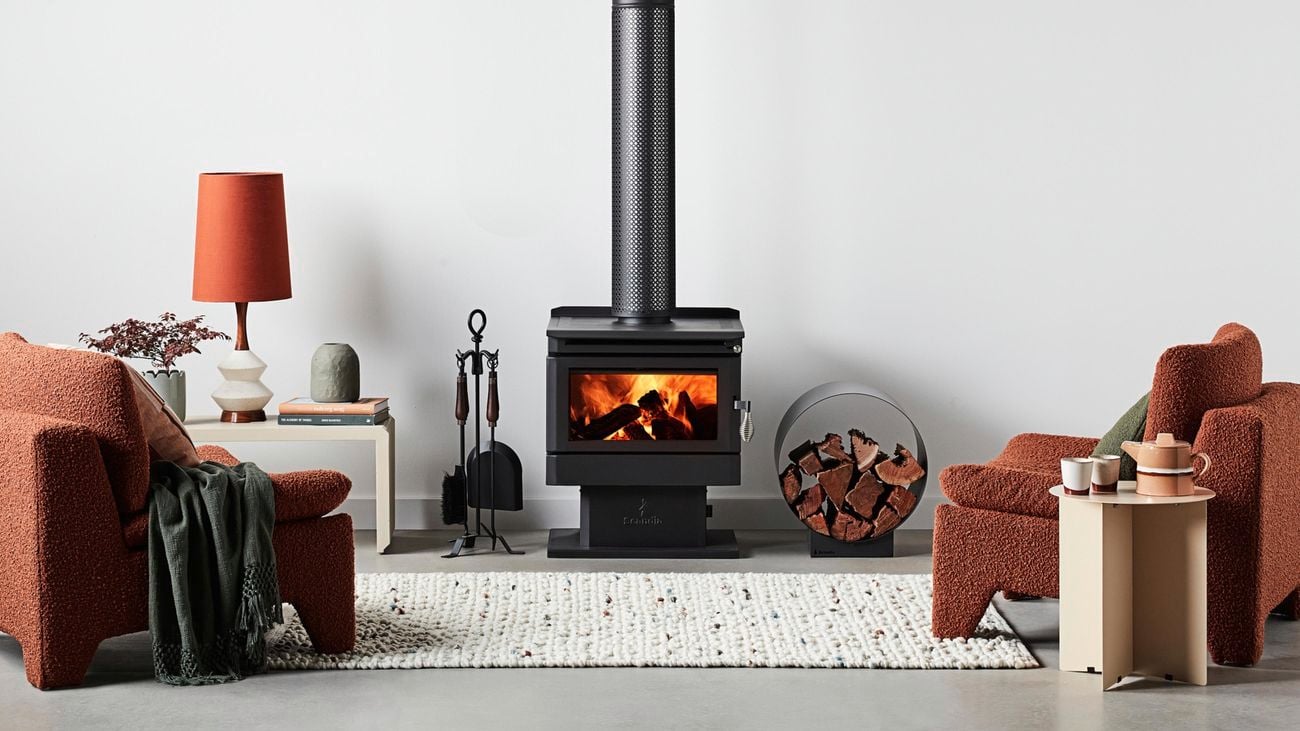 Loungroom setting with an indoor fire pit with a circular wood holder next to it and armchairs either side