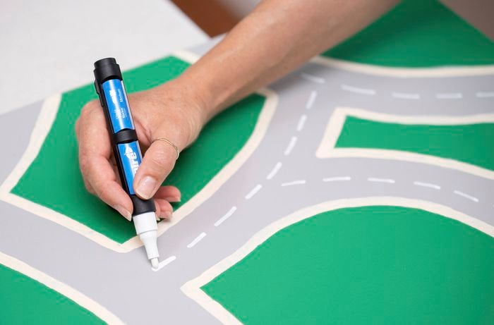 A person is drawing dashed centre lines using a white paint pen for the road markings.
