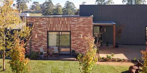 A front area of a house with trees, paving, shrubs and a grass area in it.