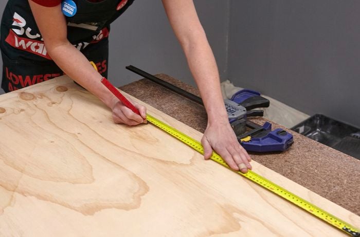 A person marking measurements on a sheet of plywood 