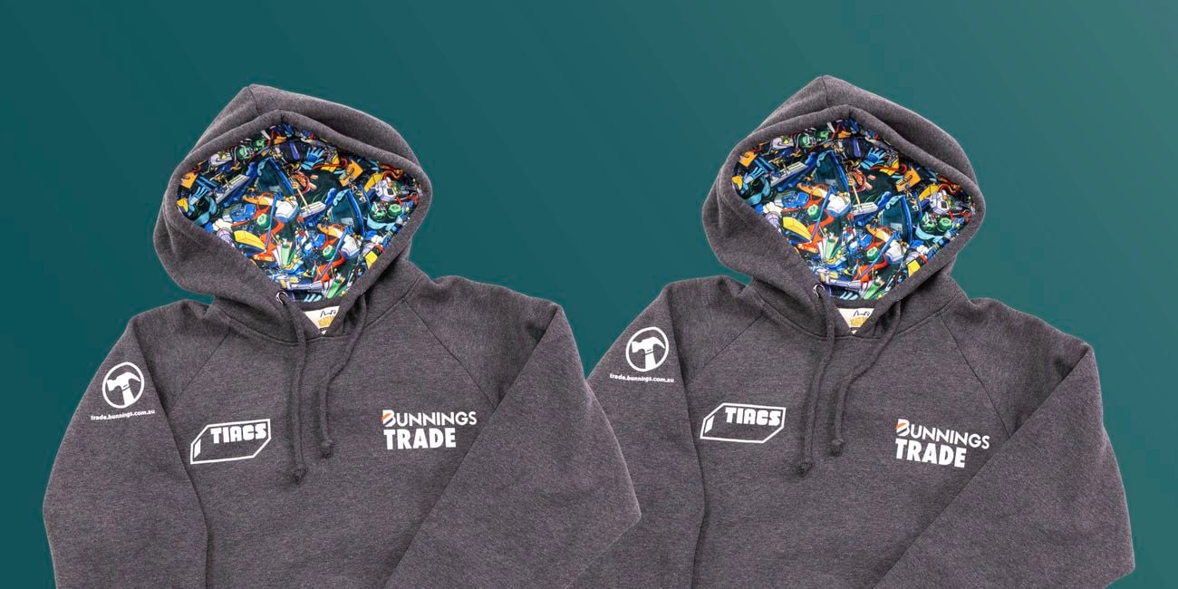 Two TIACS and Bunnings Trade branded grey hoodies on coat hangers hanging on a clothes rack.
