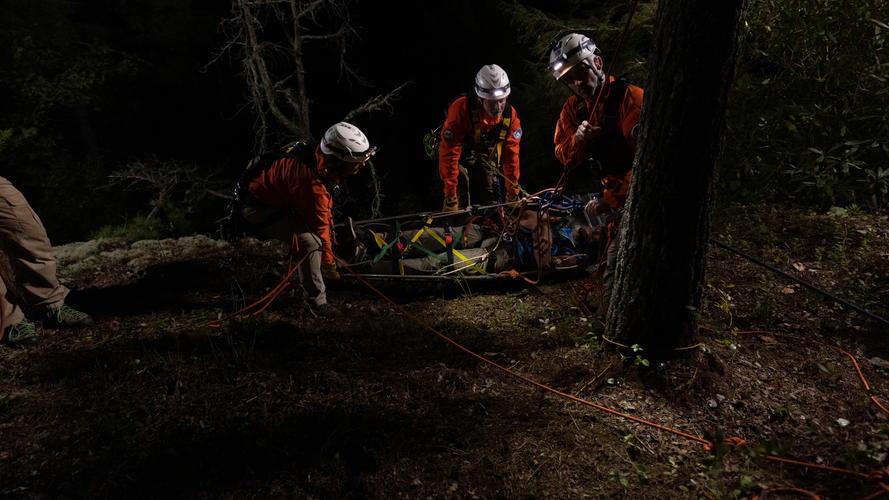 Three people in safety gear huddled around person on stretcher.