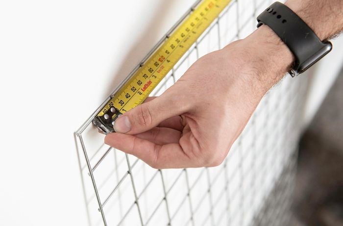 A tape measure being used to measure the width of a mesh grid