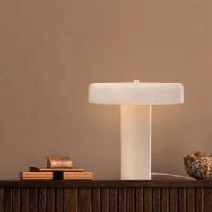 A soft-glow table lamp on a wooden sideboard, styled with decorative vases, bowls, and greenery against a warm beige wall.