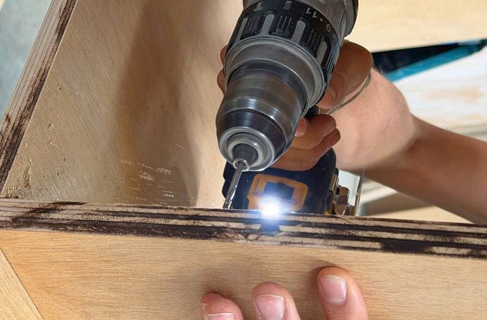 A drill being used to attach a bracket to the plywood display unit.