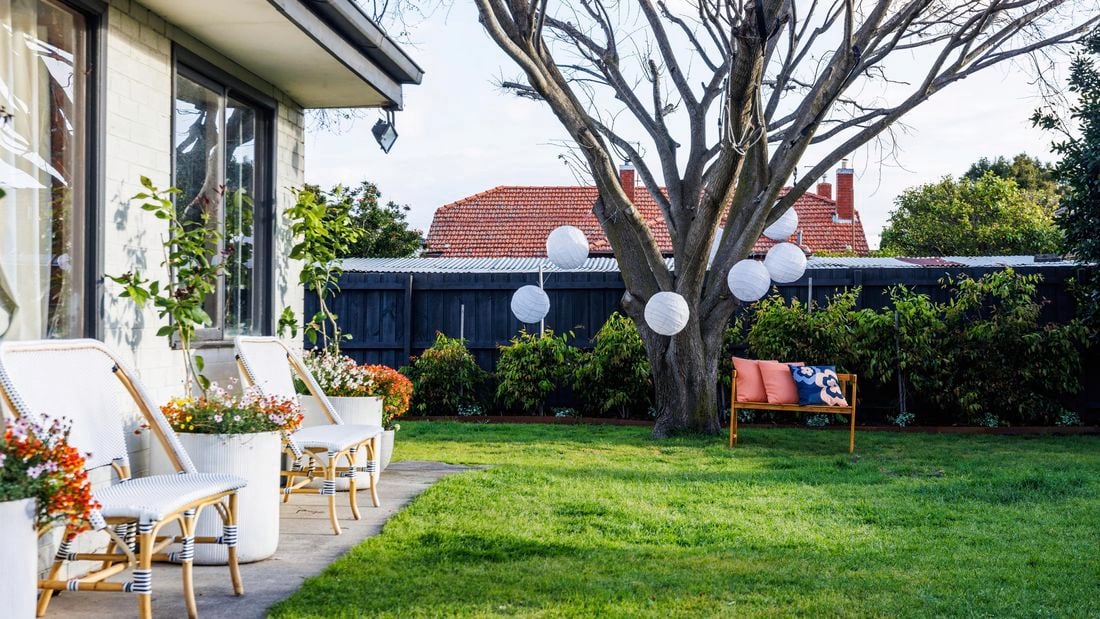 A decorated garden with some white balls, colour full flowers and two white chairs.
