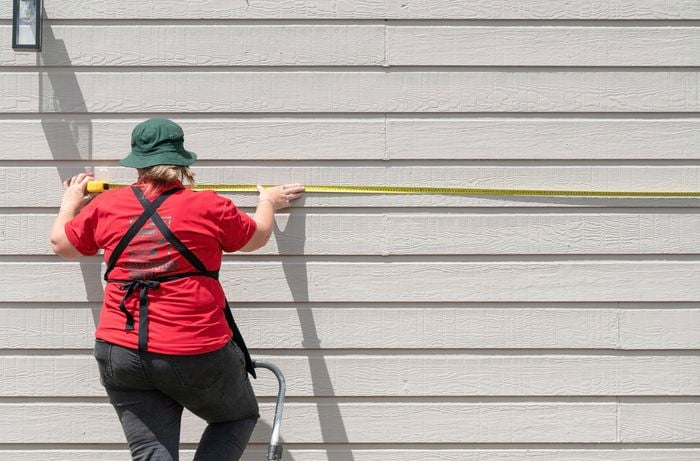 Person standing on a step ladder measuring a wall using a measuring tape
