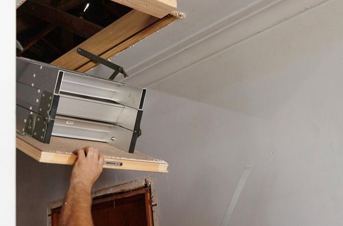 A person lifting an attic ladder into position in a hole in a ceiling