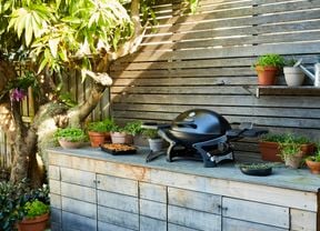A portable barbecue in an outdoor setting surrounded by pot plants with herbs