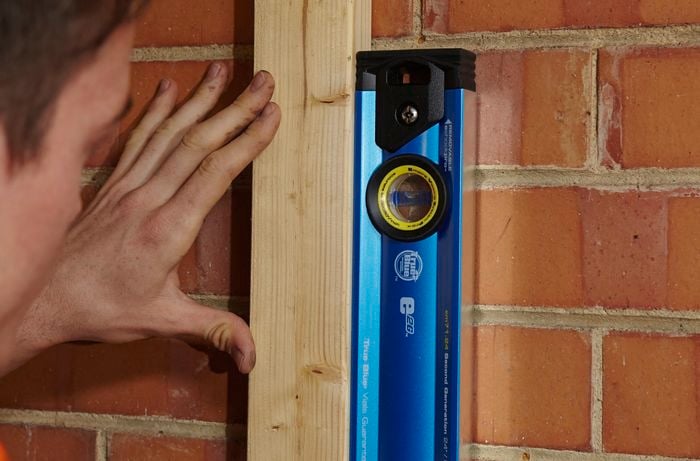 A spirit level being used to align an upright length of wood
