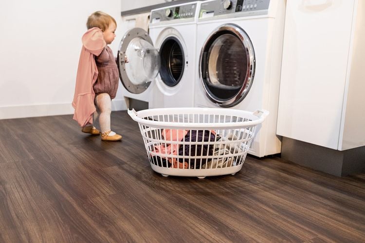 Toddler standing on a vinyl plank timber-look floor holding a piece of clothing in front of a washing machine 