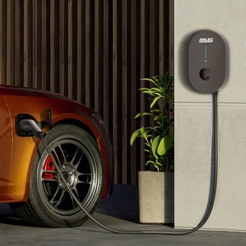 Close-up of a hand holding a black Arlec charging plug, positioned near an electric vehicle's charging port outdoors.