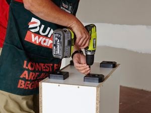 Attaching the plastic feet to the bottom of the kitchen cabinet.