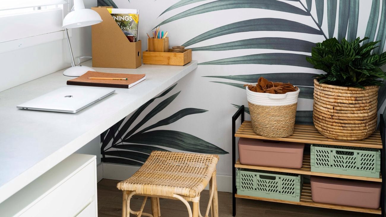 A room with a shelving unit with baskets and pot plants on it and a desk with a lap top on it