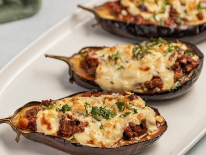 Baked eggplant halves filled with a savoury meat mixture and topped with melted golden-brown cheese on a serving platter.