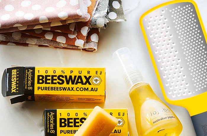 A pair of scissors, beeswax, fabric, jojoba oil, and a hand grater on a table.