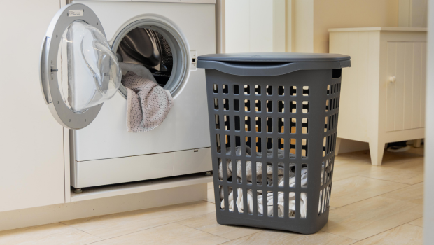 A laundry basket filled with clothes positioned beside a washing machine in a laundry room setting.