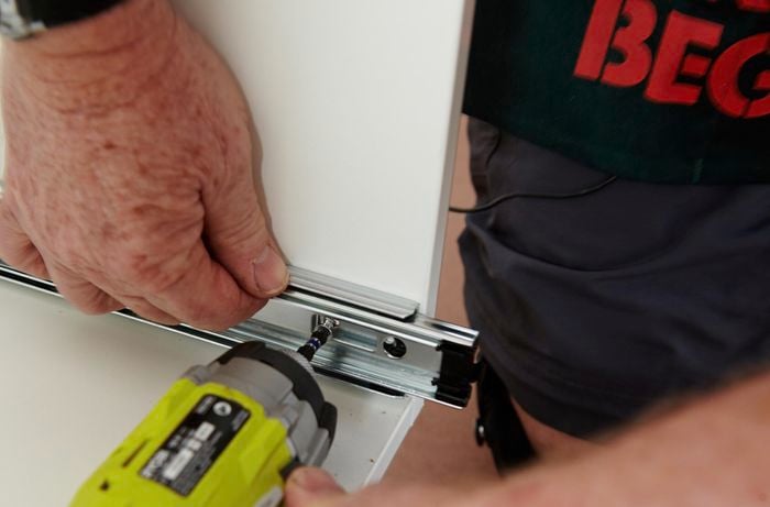 Drawer runners being secured to the inside of a kitchen cabinet using a power drill