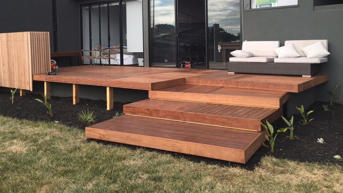 Backyard of a house with decking built on top of grass and dirt surfaces.
