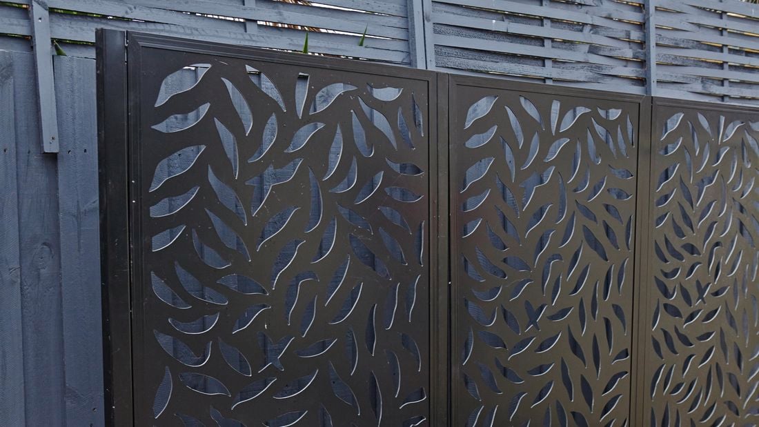 A three-panel metal screen in front of a paling fence
