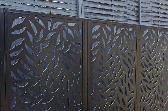 A three-panel metal screen in front of a paling fence