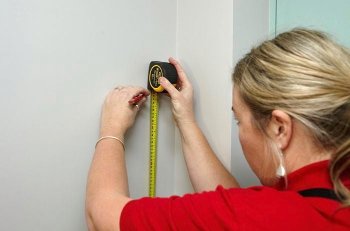 Person using measuring tape and pencil to mark up wall.