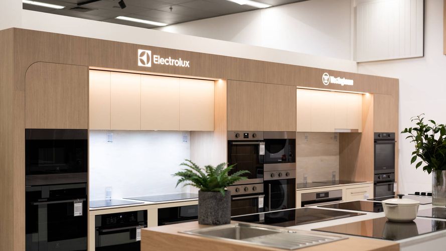 Contemporary kitchen display featuring Electrolux and Westinghouse appliances, timber cabinetry, integrated ovens and a central island bench in a showroom setting.