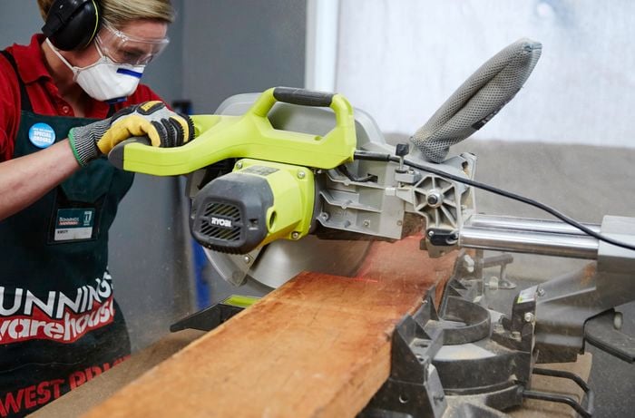 A person cutting a timber sleeper with a drop saw