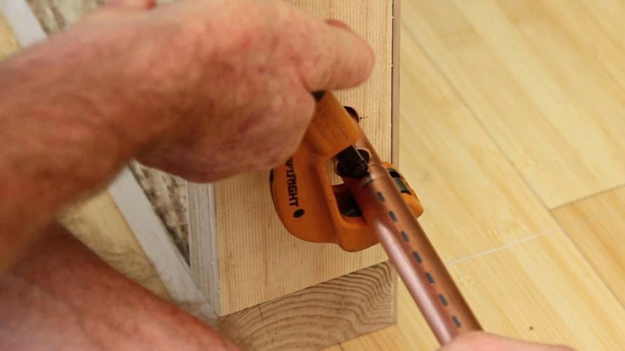 A person cutting a copper bar using a pipe cutter.