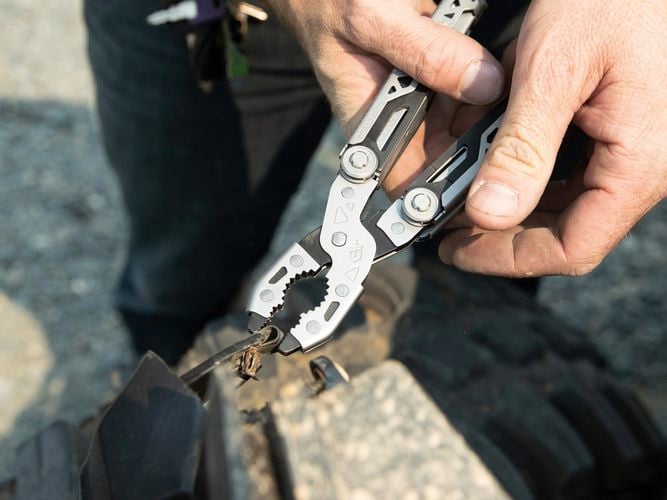 A person tightening metal strip using dual force multi tool.