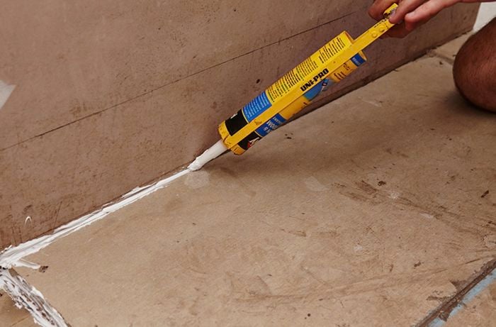 A person applying silicone between the floor and the wall in a bathroom