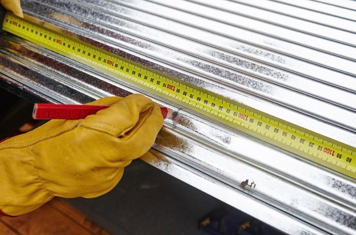 Person marking metal roof frame with pencil.