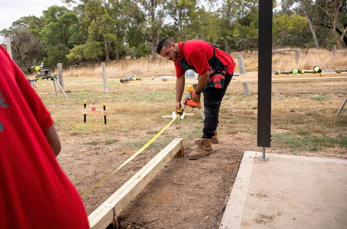 A Bunnings Team Member holding a measuring tape over a plank of wood