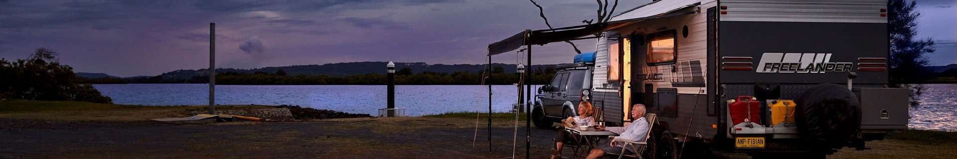 Caravan with couple sitting under awning.
